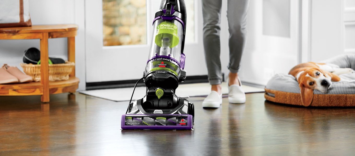 A person vacuuming with a bagless upright vacuum next to a dog in a pet bed. Links to a blog post about how to find the best vacuum for your home.